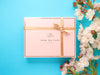 Luxury branded, pink gift box with golden ribbon, decorated with white flowers