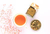 Cup with peach coloured tea, square glass jar and the loose leave tea