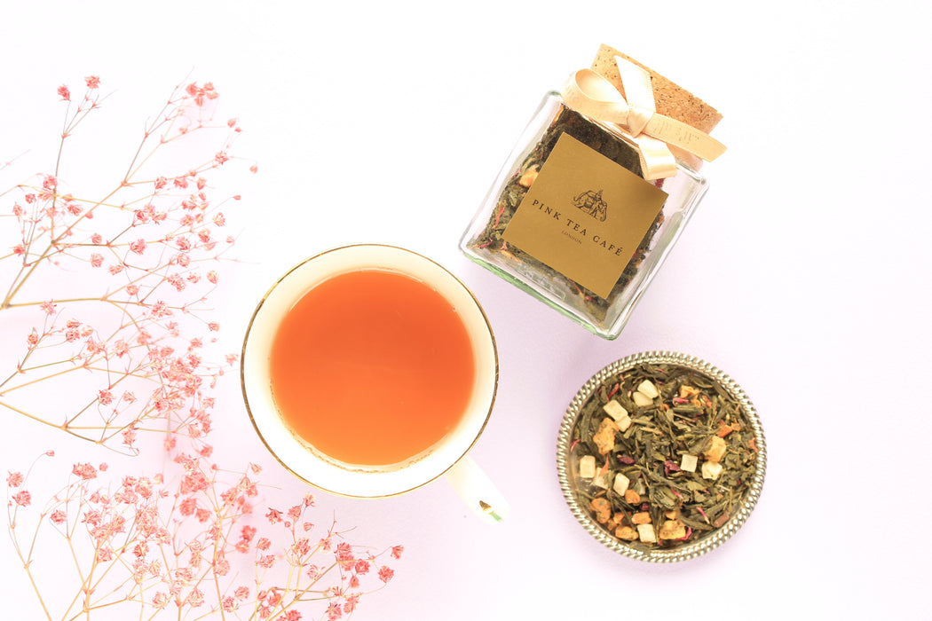 Cup with peach coloured tea, square glass jar and the loose leave tea