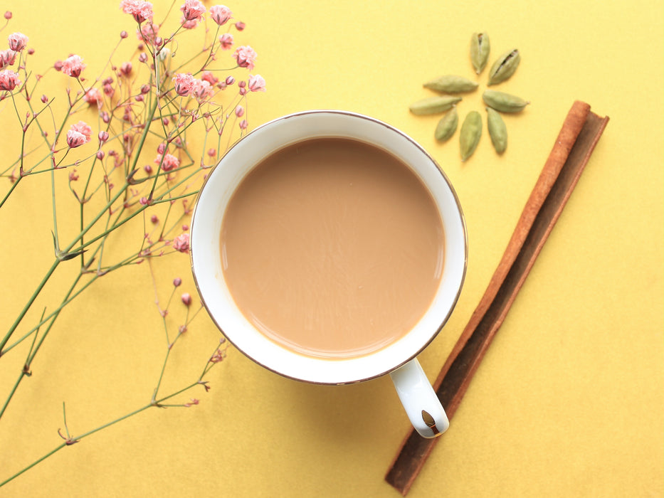 Golden chai in a cup and showing key ingredients like cinnamon and cardamom in the background