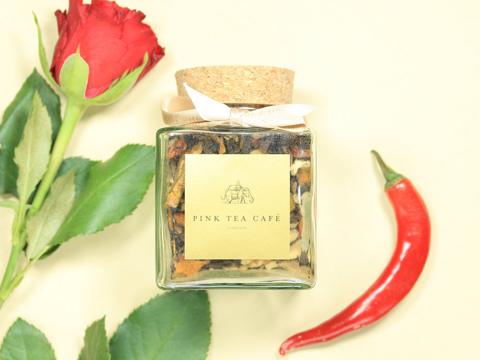 Square glass jar with golden ribbon and cork lid, decorated with a red chilli and a red rose
