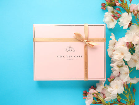 Luxury branded, pink gift box with golden ribbon, decorated with white flowers